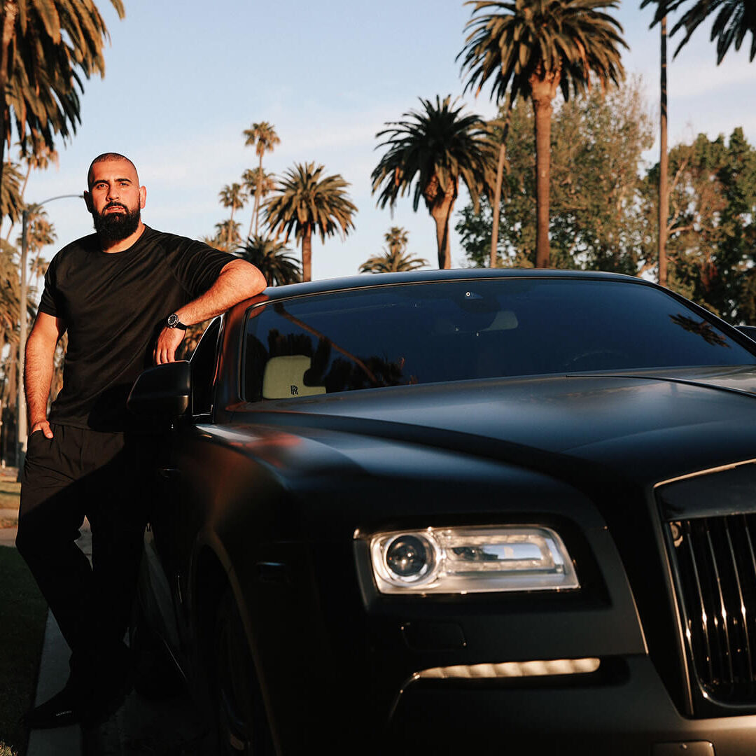 Farshad Dehbozorgi chilling with his car with palm trees in the background